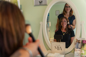 Frau wird mit Puderpinsel geschminkt - Reflektion im Spiegel.